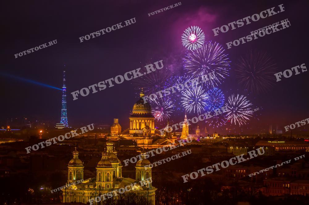 На фотографии изображен фейерверк над Санкт-Петербургом. Видны Исаакиевский собор и Никольский собор в вечернее время. Фото может использоваться для праздничных открыток, туристических буклетов и рекламных материалов.